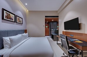 Ein Hotelzimmer mit einem Bett, einem Schreibtisch, einem Sessel, einem Fernseher und gerahmten Bildern an der Wand.