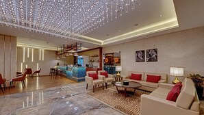 A spacious lobby with a marble floor, a seating area with sofas and chairs, a bar area, and a ceiling with hanging lights. - The Neemaya Hotel (Gandhidham)