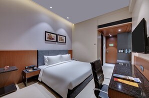 Ein modernes Hotelzimmer mit einem ordentlich bezogenen Bett, einem Schreibtisch mit Stuhl, einem Flachbildfernseher und einer kleinen Küchenzeile.