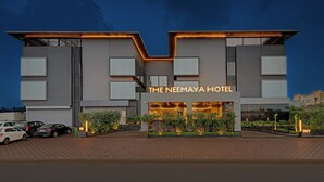 The Neemaya Hotel with a modern architectural design, featuring a prominent entrance and a parking area in front. - The Neemaya Hotel (Gandhidham)