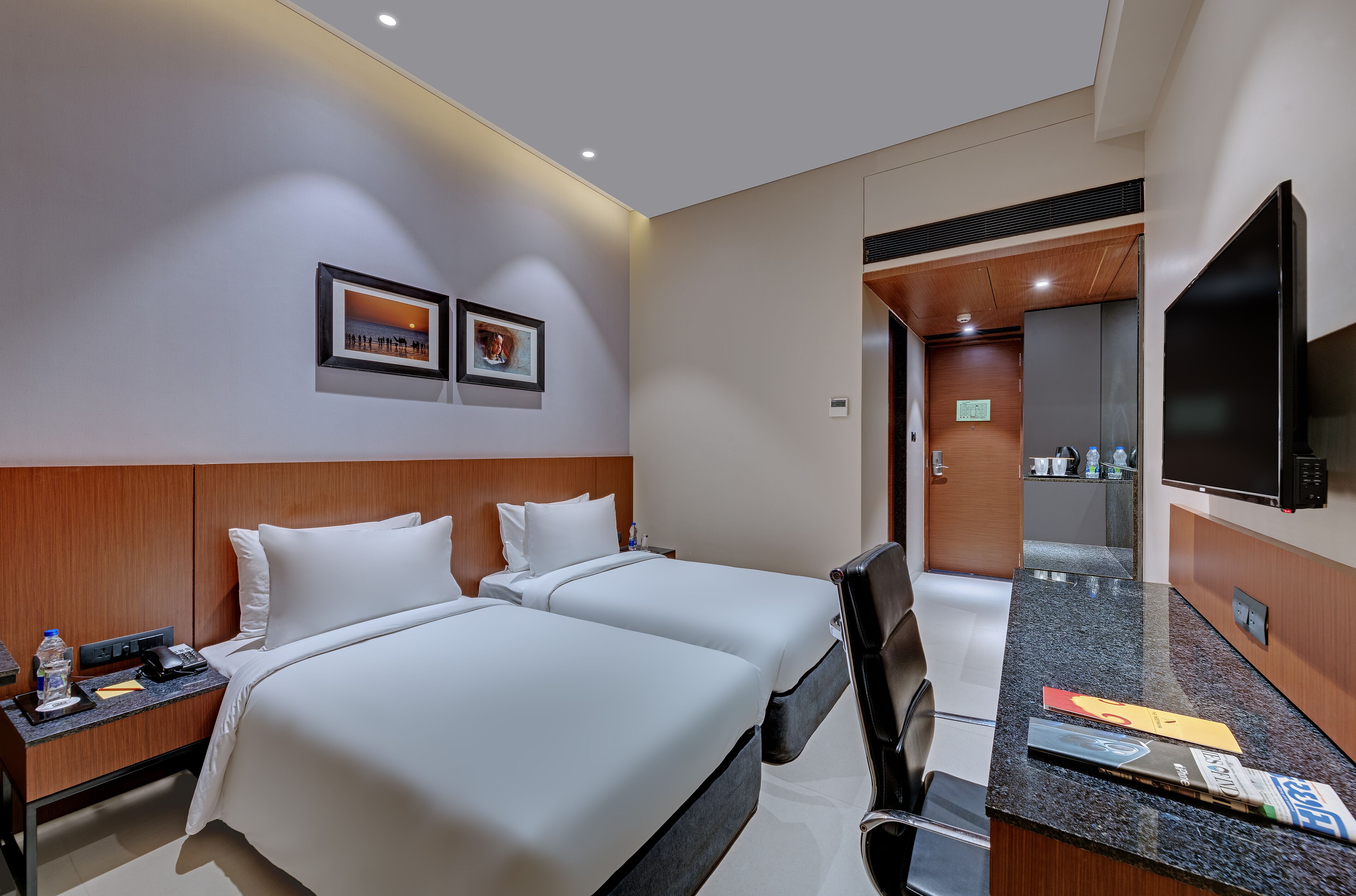 Une chambre d’hôtel avec deux lits, un téléviseur à écran plat, un bureau avec une chaise et une salle de bain visible à travers une porte ouverte.