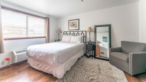 Um quarto com cama, mesas de cabeceira, uma cadeira, um espelho e janela com persianas.