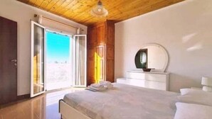 Een slaapkamer met een houten plafond, een groot bed, een nachtkastje met spiegel en uitzicht door een schuifdeur.