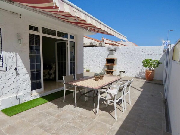 A patio with a table and chairs, a grill, and a potted plant.