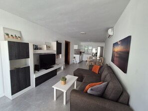 A modern living room with a flat-screen TV, a sofa, and a dining area in the background.
