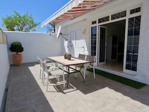 Un patio con tavolo e sedie, un vaso con una pianta e una porta scorrevole in vetro che dà su un ambiente interno.