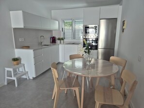 A modern kitchen with white cabinets, a stainless steel refrigerator, and a dining table with chairs.