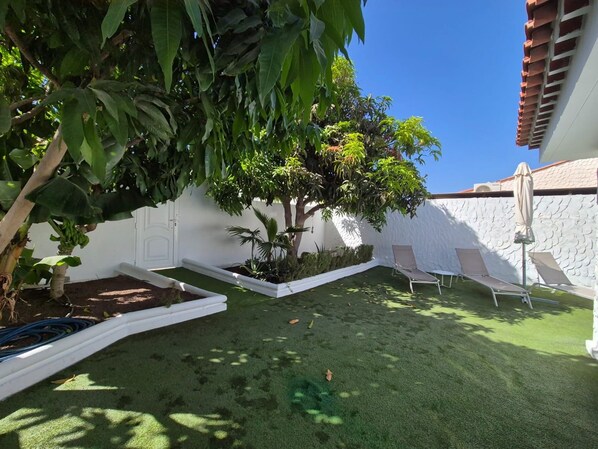 Un jardín cuidado con un árbol, un muro blanco y un techo de tejas.