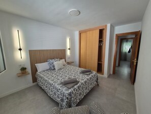 A bedroom with a bed, bedside tables, a wardrobe, and a hallway leading to another room.