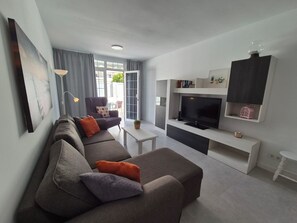 A modern living room with a sofa, a flat-screen TV, and a dining area.