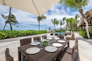 An outdoor dining area with wicker tables and chairs, a pool, and palm trees. - Two Ocean View Caleton Villas in CapCana (Punta Cana)