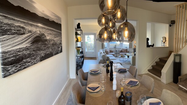 Uma sala de jantar com uma mesa comprida posta para seis pessoas, um lustre moderno e um grande quadro abstrato na parede.