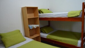 Habitación con literas, una estantería de madera y ropa de cama verde.