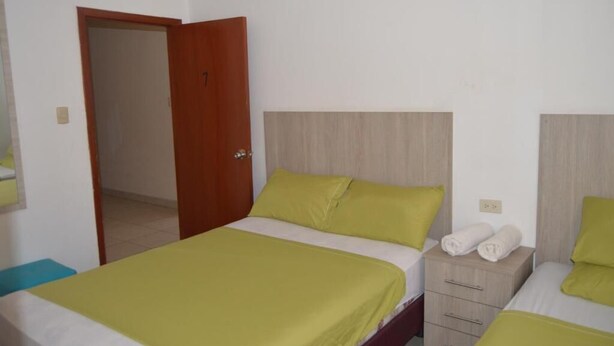 Habitación de hotel con dos camas, una puerta de madera y una mesita de noche pequeña con toallas.