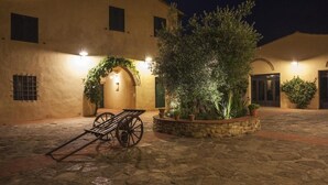 A courtyard with a stone floor, a wooden cart, and a building with a lighted entrance. - Torriano 2 (San Casciano Val di Pesa)