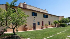 A building with a tiled roof, a stone wall, and a well-maintained lawn with stepping stones. - Torriano 2 (San Casciano Val di Pesa)