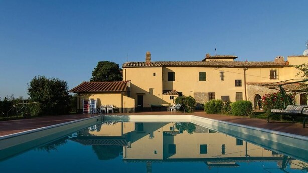 A swimming pool with a reflection of a building and trees. - Torriano 2 (San Casciano Val di Pesa)