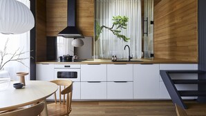 A modern kitchen with wooden cabinetry, a black range hood, a sink with a black faucet, and a dining area with a round table and chairs. - The Ryokan - Zen (Manly)