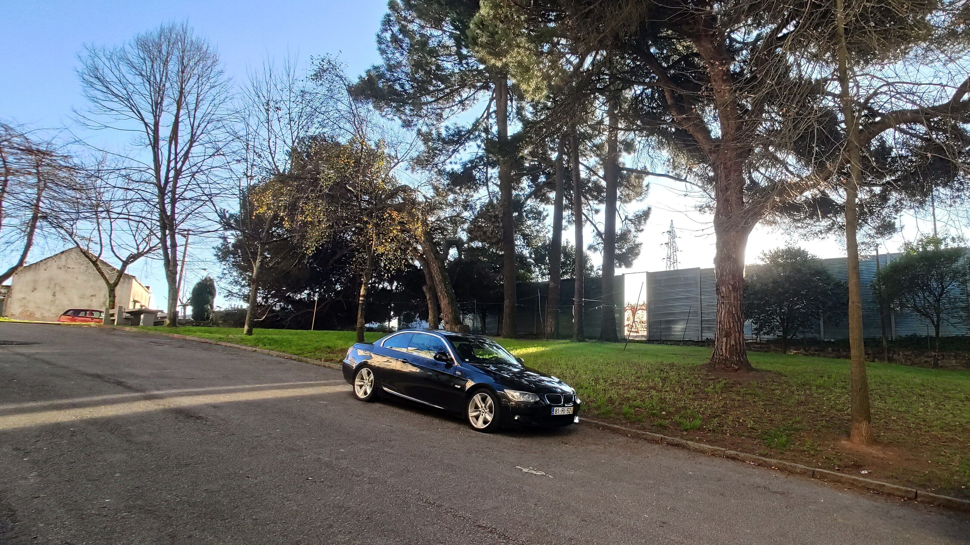 A black car parked on a street with trees and a building in the background.
