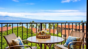 Un balcón con mesa y sillas, con vistas a la costa, edificios y palmeras.