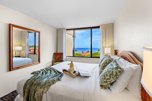 A hotel room with a large bed, a bedside table, a mirror, and a window with a view of the ocean.