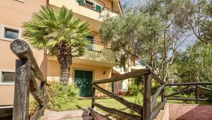 A wooden staircase leading to a building with a green door, surrounded by greenery and a palm tree. - I Mirti Bianchi Residence con piscina (Santa Teresa di Gallura)