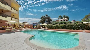 A swimming pool with lounge chairs and umbrellas, surrounded by a tiled deck and a building with balconies. - I Mirti Bianchi Residence con piscina (Santa Teresa di Gallura)