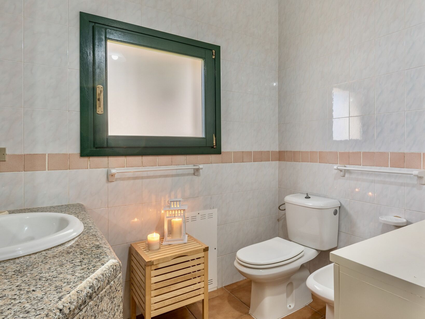 Une salle de bain avec un lavabo en granit, un tabouret en bois orné de bougies, des toilettes et un miroir avec un cadre vert.