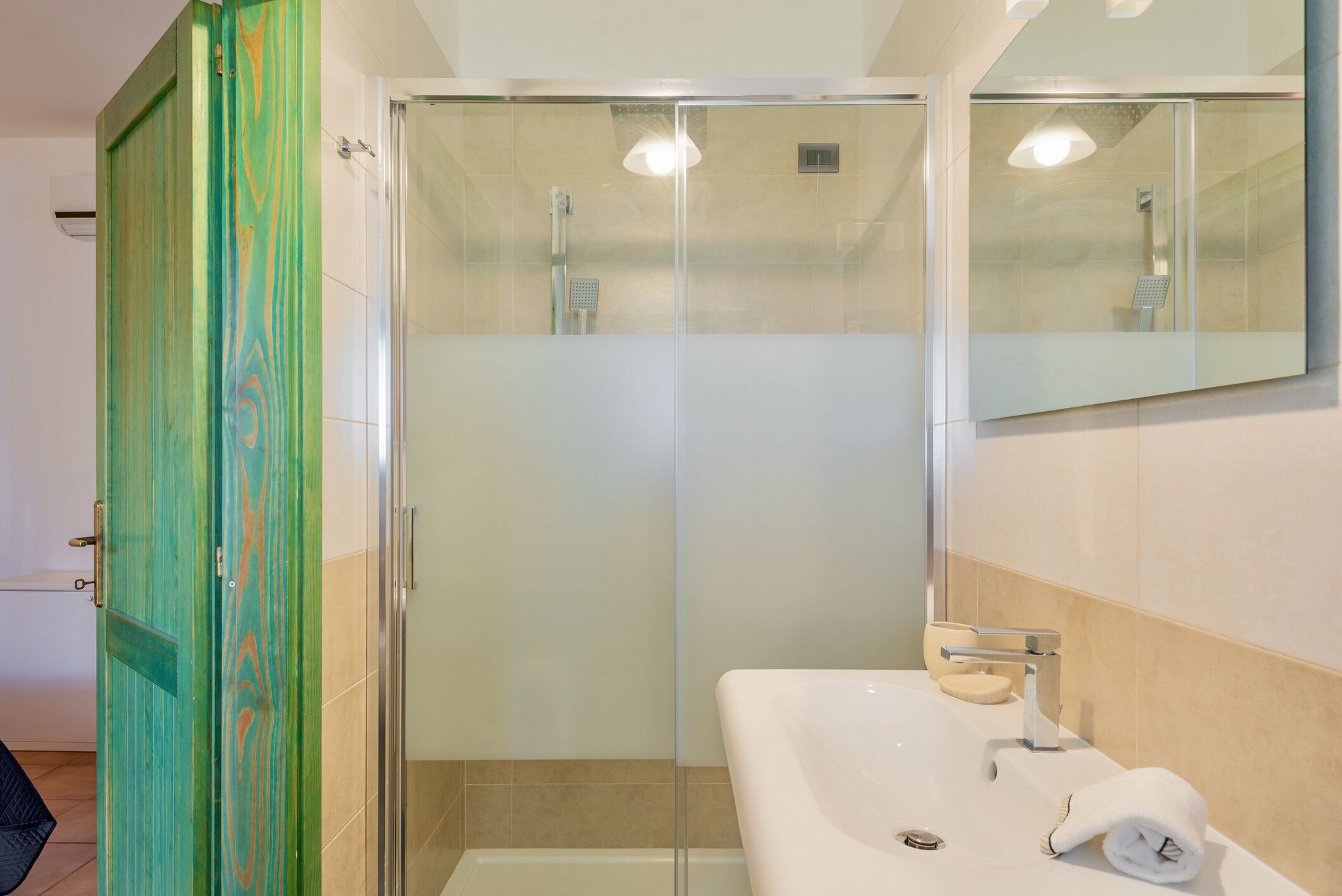 A modern bathroom with a glass shower enclosure, a white sink with a soap dish, and a towel on the counter.