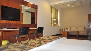 Ein Hotelzimmer mit einem Bett, einem Schreibtisch mit Flachbildfernseher, zwei Stühlen, einem Sofa und einem Fenster mit Jalousien.