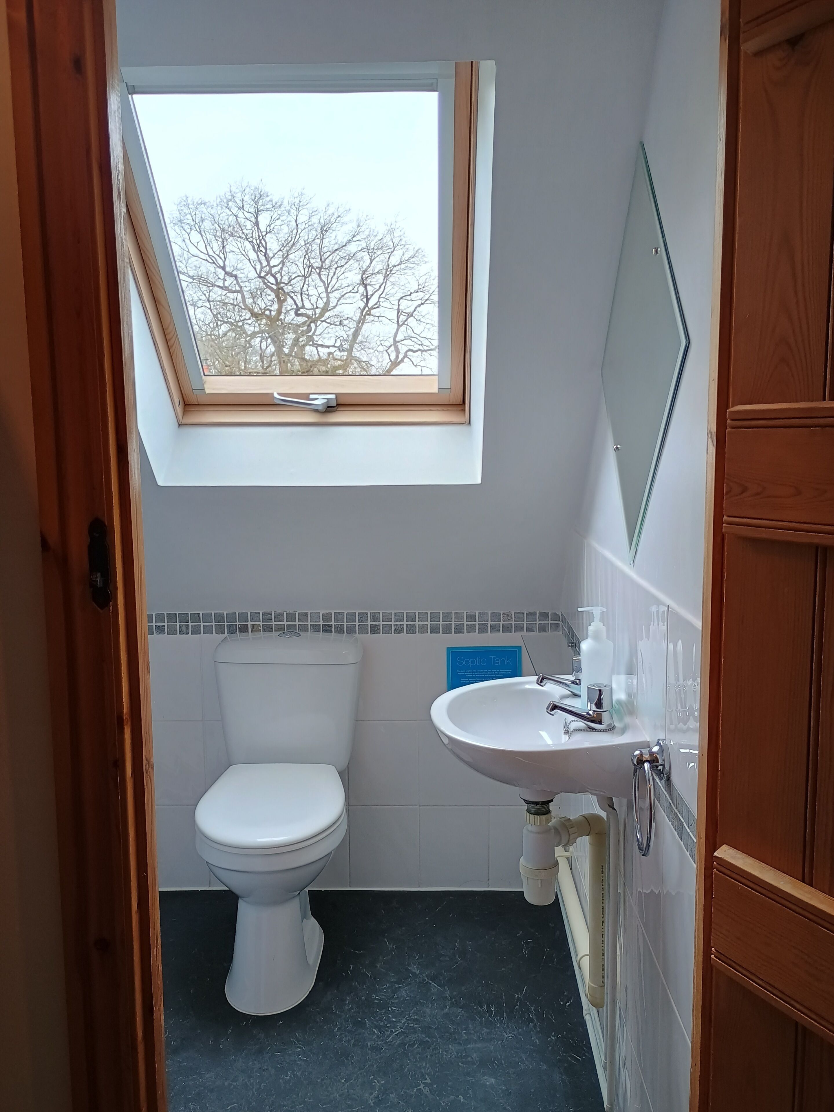 Ein kleines Badezimmer mit Dachfenster, Toilette, Waschbecken und Spiegel.
