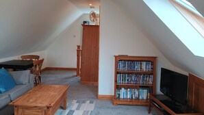 A loft-style living room with a high ceiling, a wooden bookshelf, a television, a dining table, and a sofa.