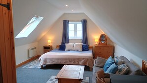 A bedroom with a bed, bedside tables, a dresser, a wooden table, a sofa, a window with curtains, and a skylight.