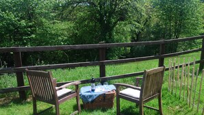 A picnic setup with two wooden chairs and a wicker basket on a grassy area, surrounded by a wooden fence.