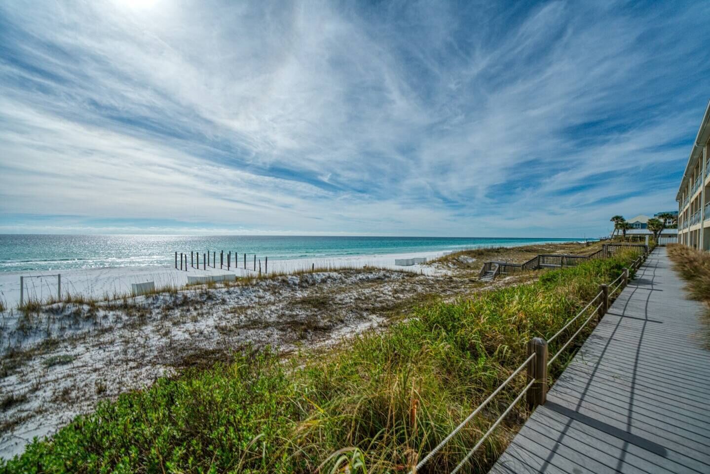 A coastal walkway with a wooden boardwalk, beach, and ocean view.
