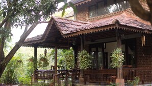 A traditional wooden house with a tiled roof, surrounded by lush greenery and a stone staircase leading to the entrance. - Amã Stays & Trails Asanji Wadi (Alibag)