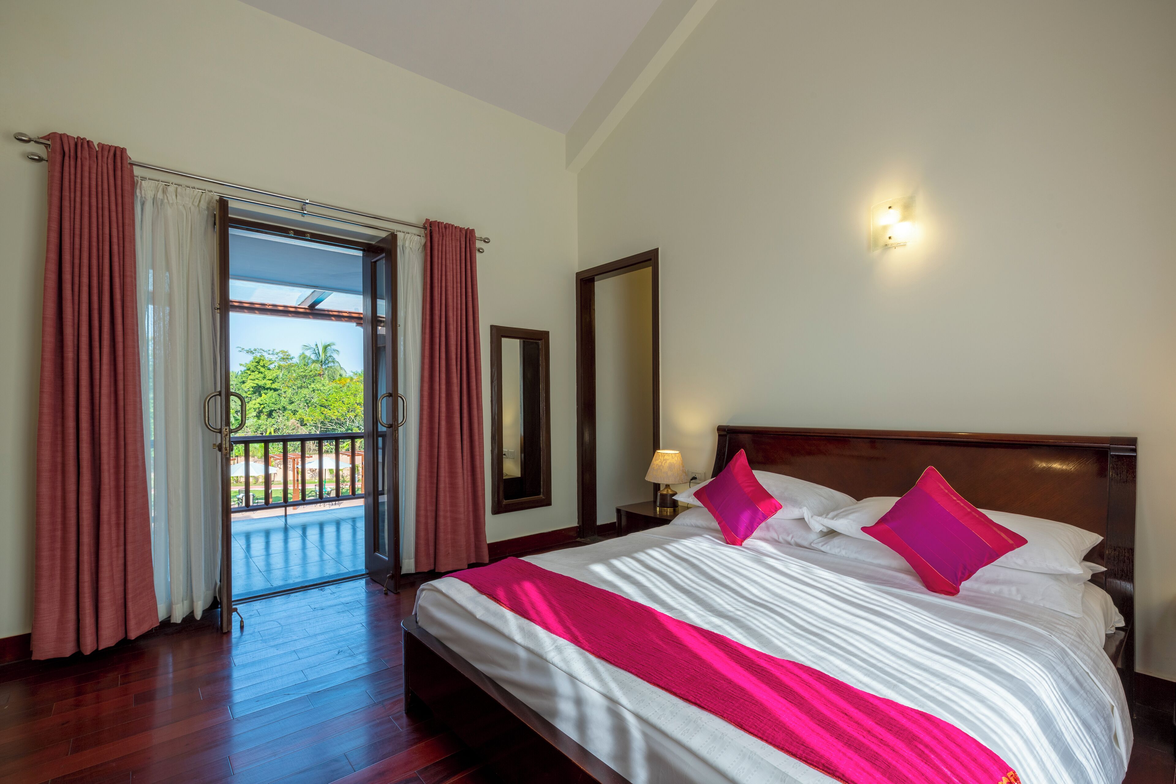 Habitación de hotel con una cama grande, una mesita de noche, una lámpara y vistas al exterior.