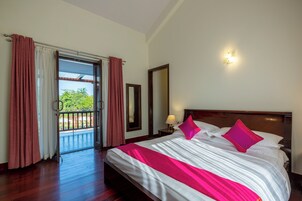 Habitación de hotel con una cama grande, una mesita de noche, una lámpara y vistas al exterior.