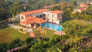 Une maison à deux étages avec une piscine, entourée d’une végétation luxuriante et de palmiers.