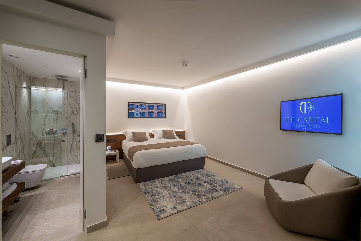 A modern hotel room with a bed, a TV, a shower, and a bathroom.