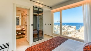 Un dormitorio con un ventanal grande que ofrece vistas a la ciudad, un armario empotrado y un baño con lavamanos de mármol.