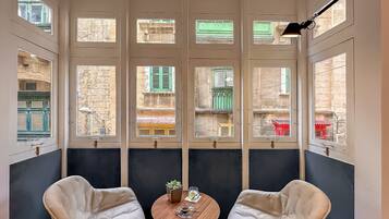 A room with two chairs, a small table, and large windows with views of buildings.