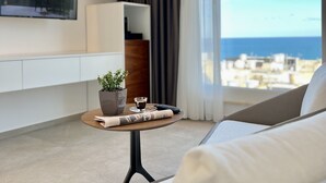 Una sala moderna con un sofá, una mesita con una planta y una taza, un televisor montado y vistas de la ciudad a través de amplias ventanas.