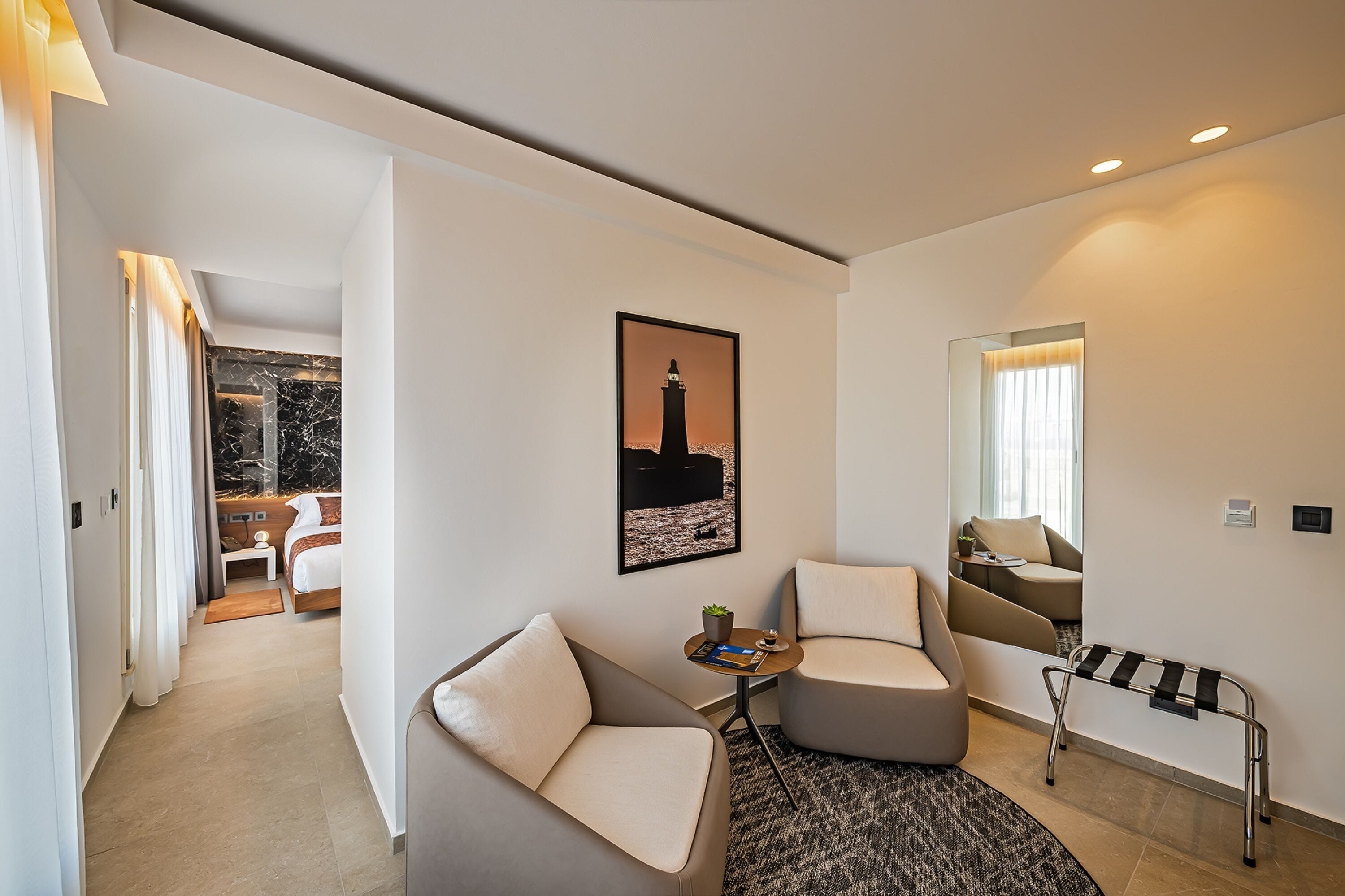Una habitación de hotel moderna con una cama, un sofá, una mesita con una planta y una imagen de un faro.
