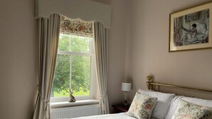 Una cama bien hecha con almohadones florales, un cabecero con marco dorado y una ventana con cortinas.