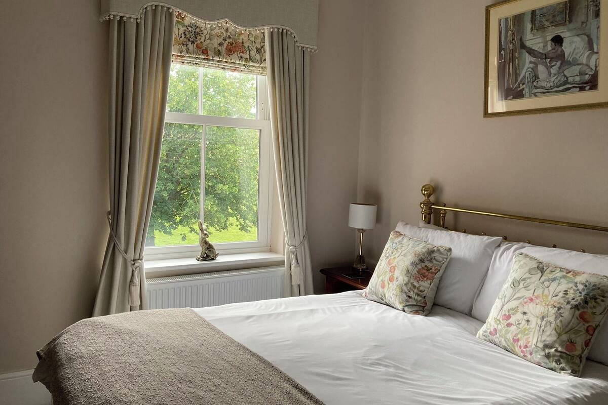 A neatly made bed with floral pillows, a gold-framed headboard, and a window with curtains.