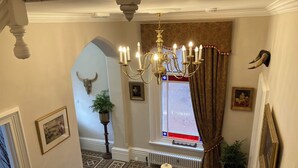Una imponente escalera con un candelabro, un ventanal con cortinas y una cabeza de toro montada en la pared.