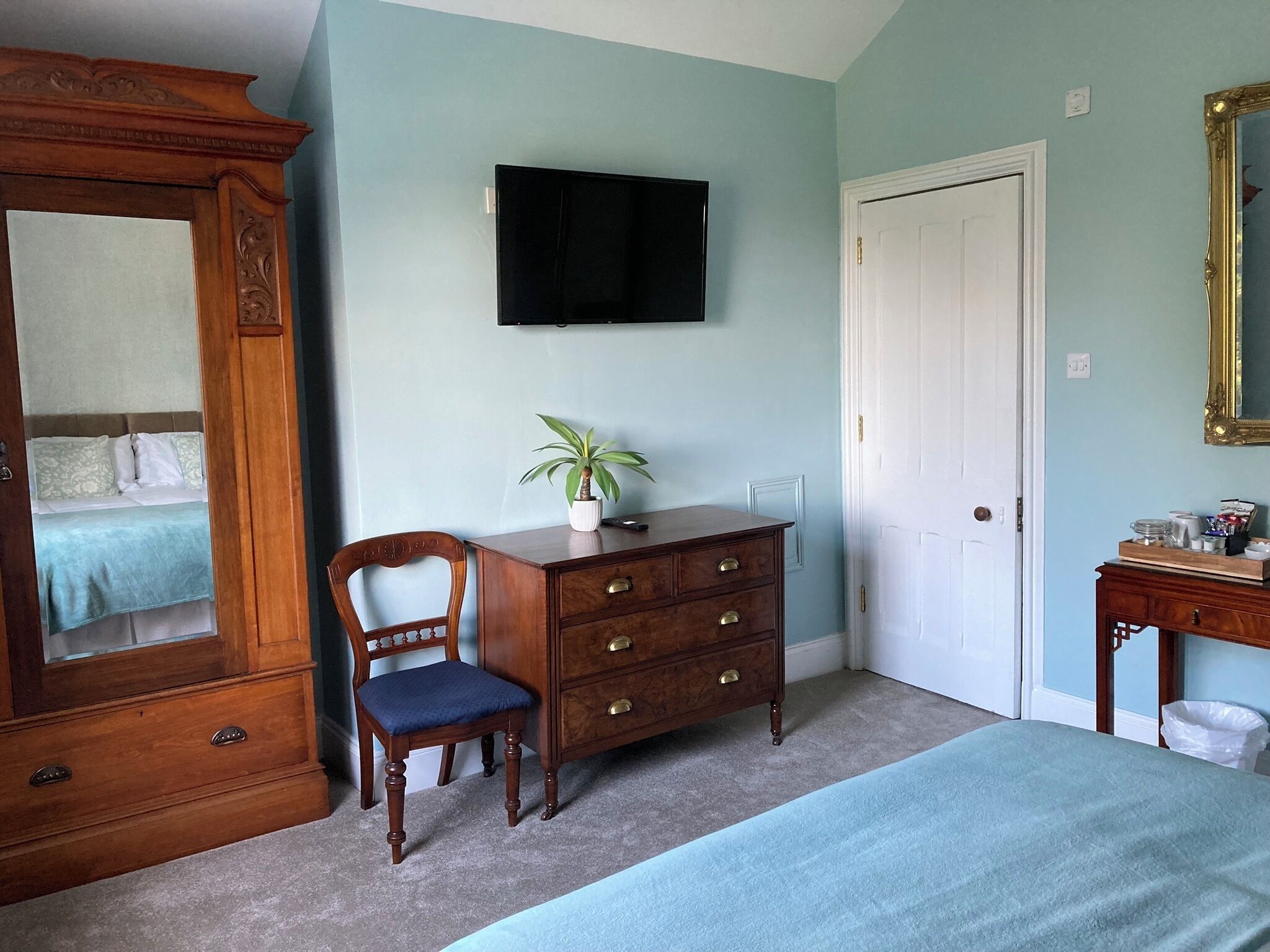 A bedroom with a bed, a dresser, a chair, a desk, a television, and a door.