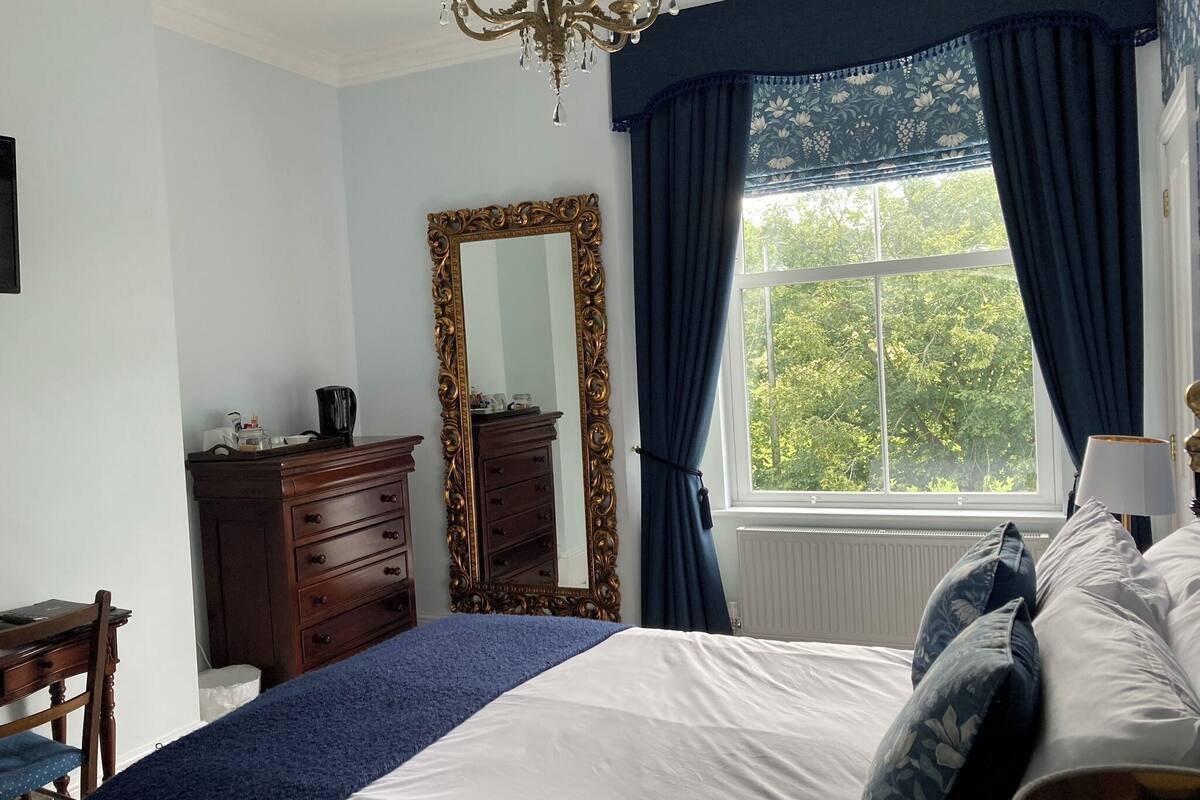 A bedroom with a large bed, a dresser, a mirror, and a window with curtains.