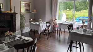 Comedor con mesas dispuestas para cuatro, chimenea, un espejo grande y vista a una piscina.